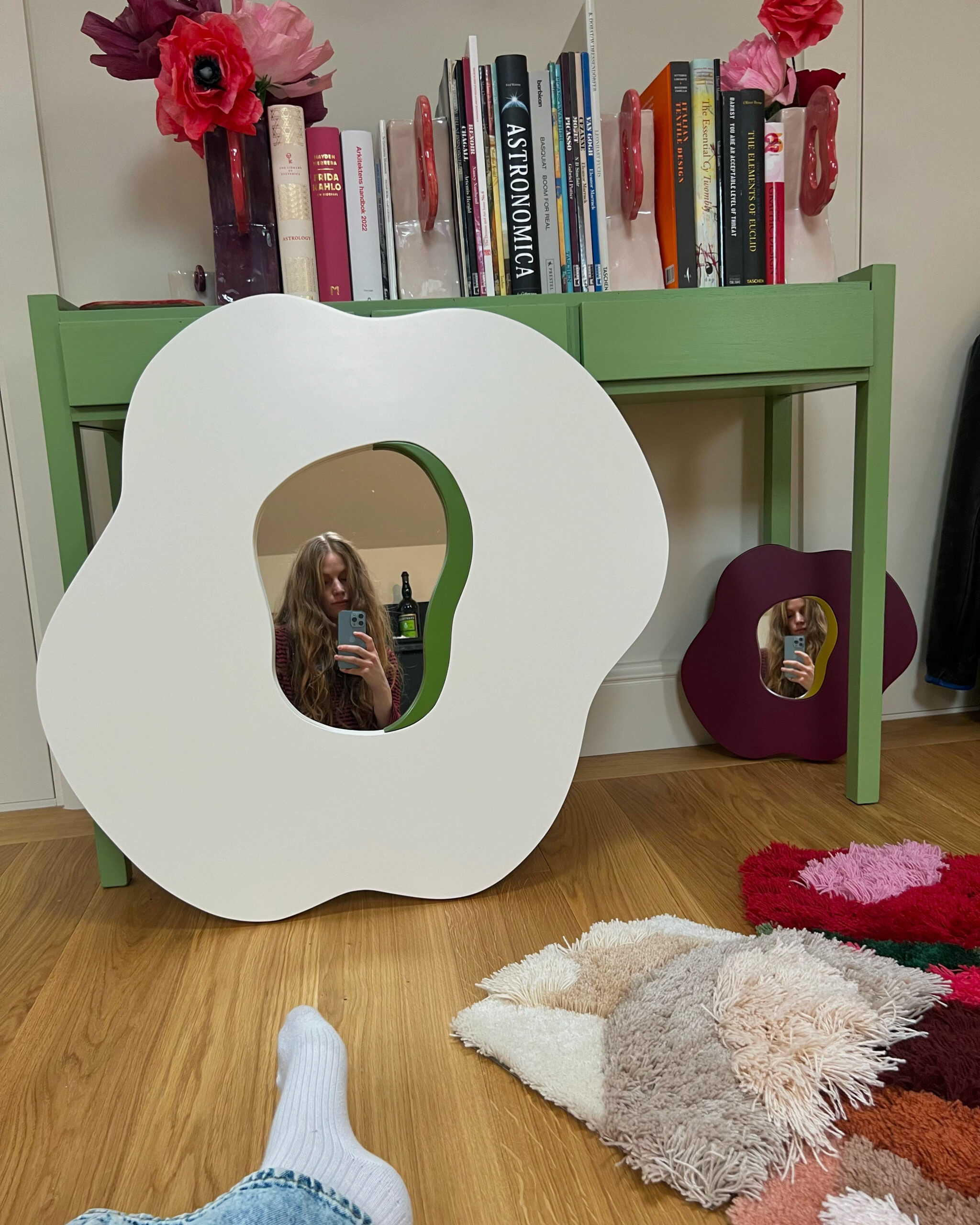 White and grass green poppy mirror standing against bookstand in studio