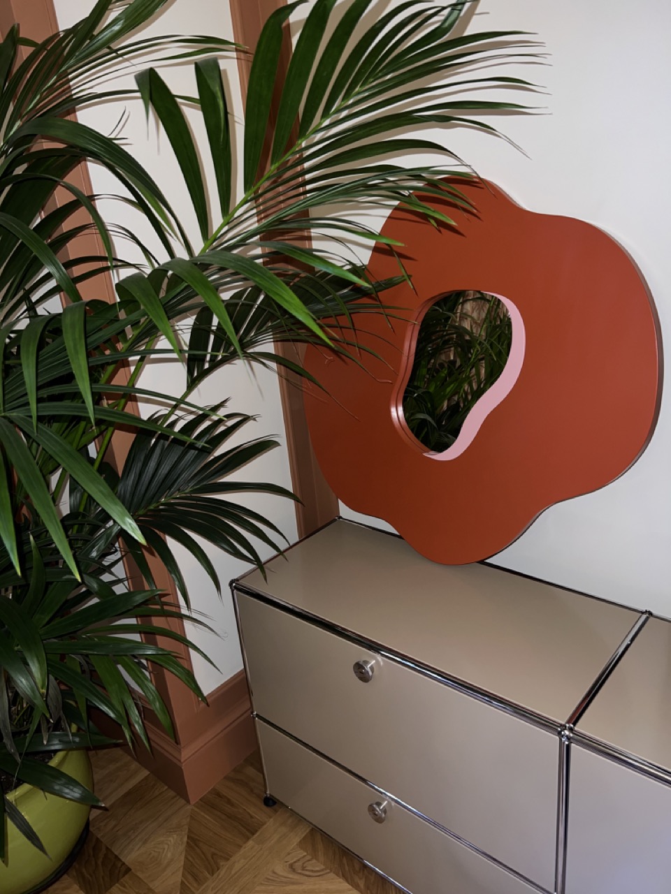 Red and pink poppy mirror standing on a shelf behind a palm tree