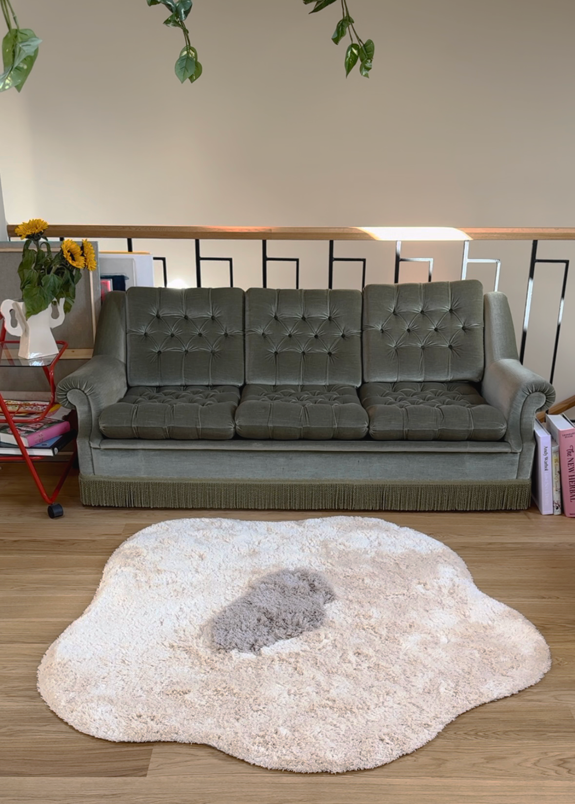 A Single Poppy Rug in creamy white in front of a green vintage sofa.